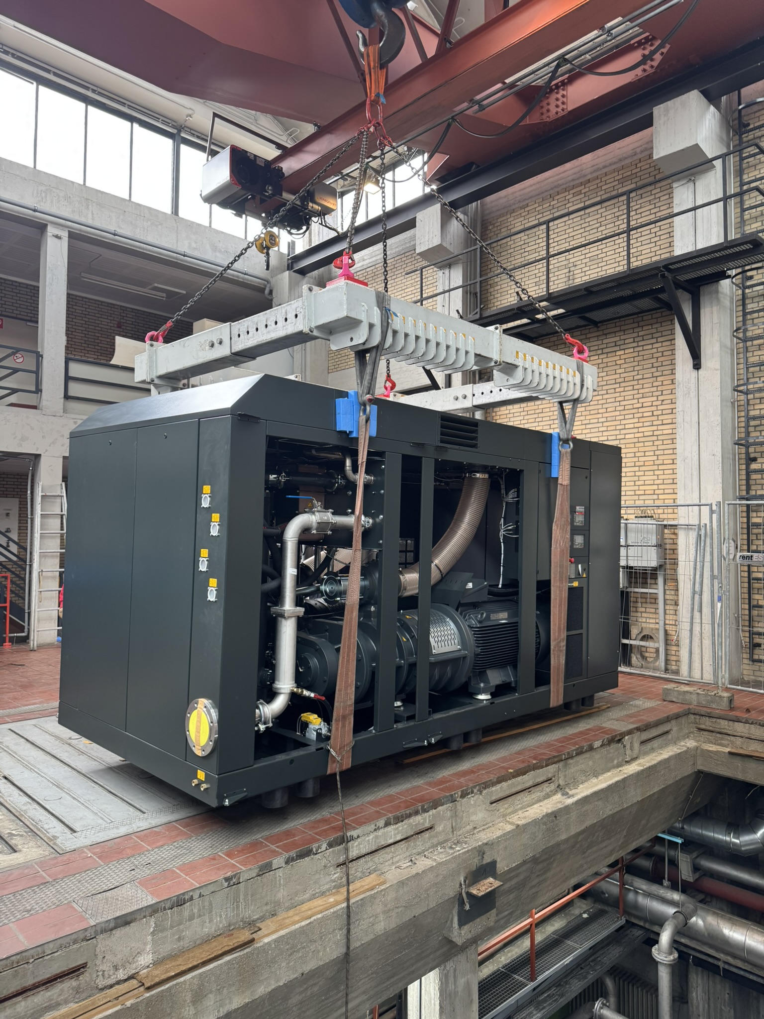 Kompressor wird mit Kran in einer Industriehalle positioniert.